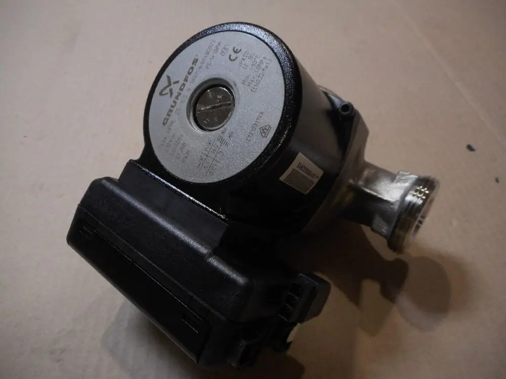 Circulating pump von Remeha, montiert auf einer Unterlage. Das Gerät hat eine runde, flache Oberseite mit einem Anschluss an einer Seite und einem elektrischen Anschluss.